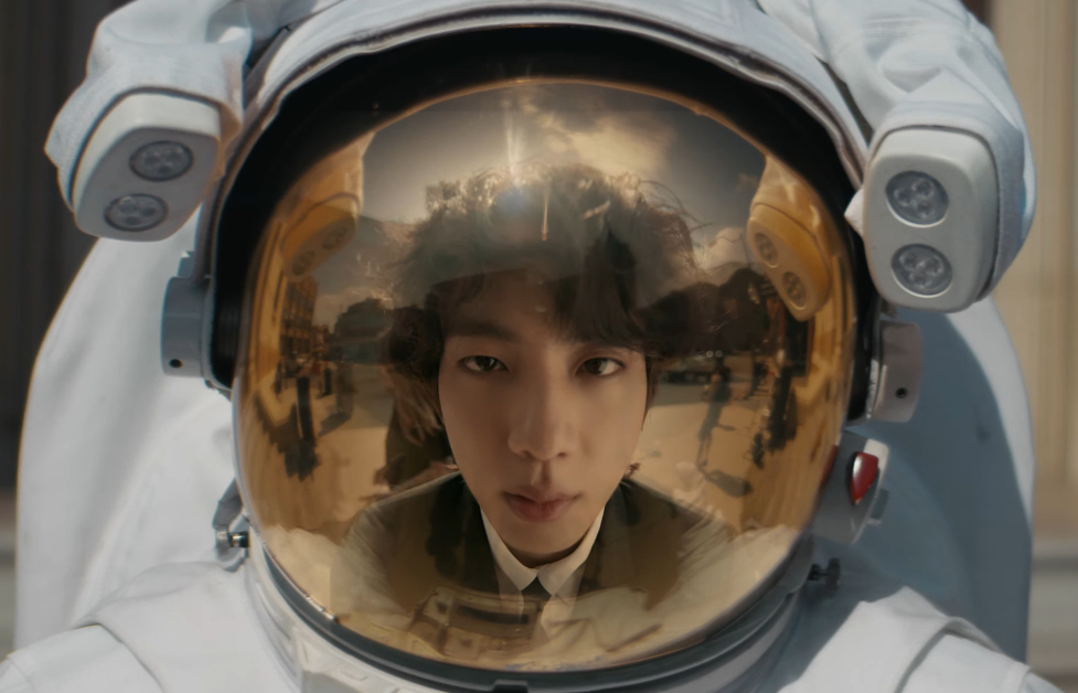 Jin (BTS) looking into a Spacesuit helmet and seeing his reflection