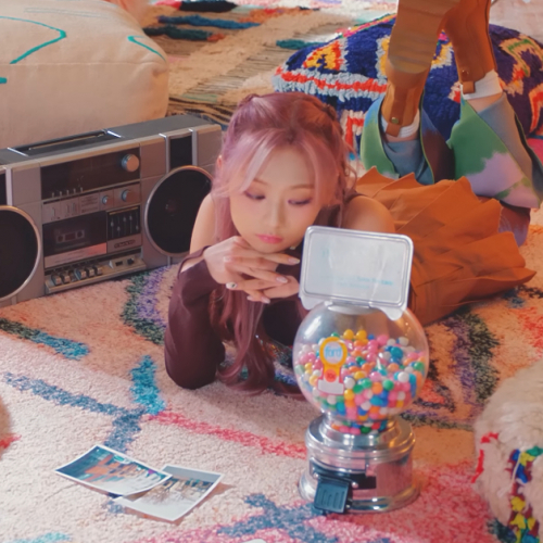 A Korean girl woman is laying on the floor next to a boombox, looking at a mini-gumball machine