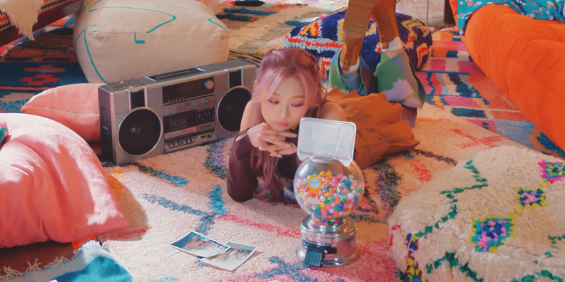 A Korean girl woman is laying on the floor next to a boombox, looking at a mini-gumball machine