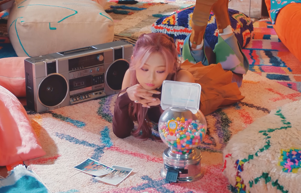 A Korean girl woman is laying on the floor next to a boombox, looking at a mini-gumball machine