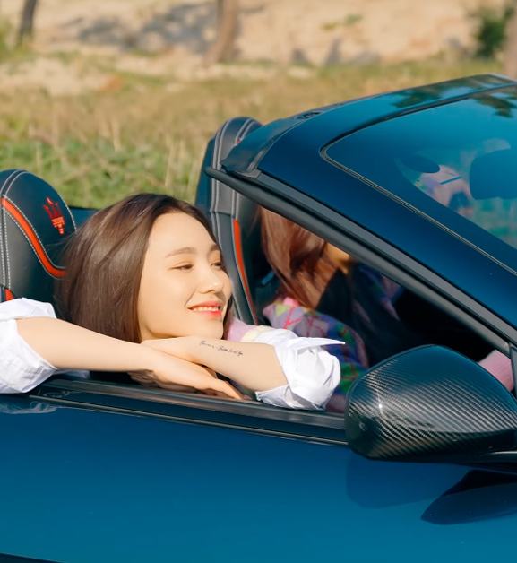 A Korean woman is resting her head on her arms on the top of the passenger door of a convertible