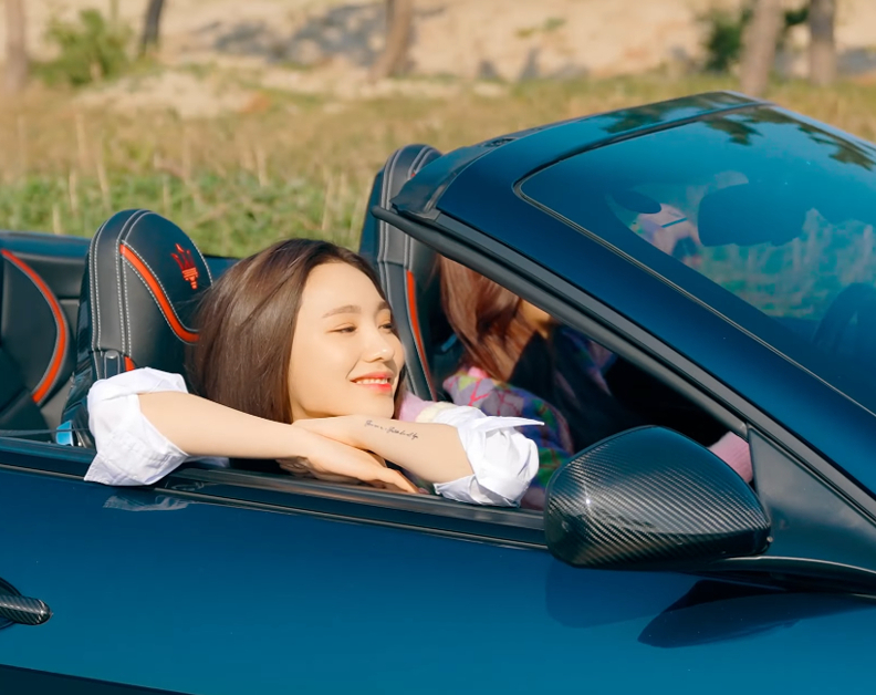 A Korean woman is resting her head on her arms on the top of the passenger door of a convertible