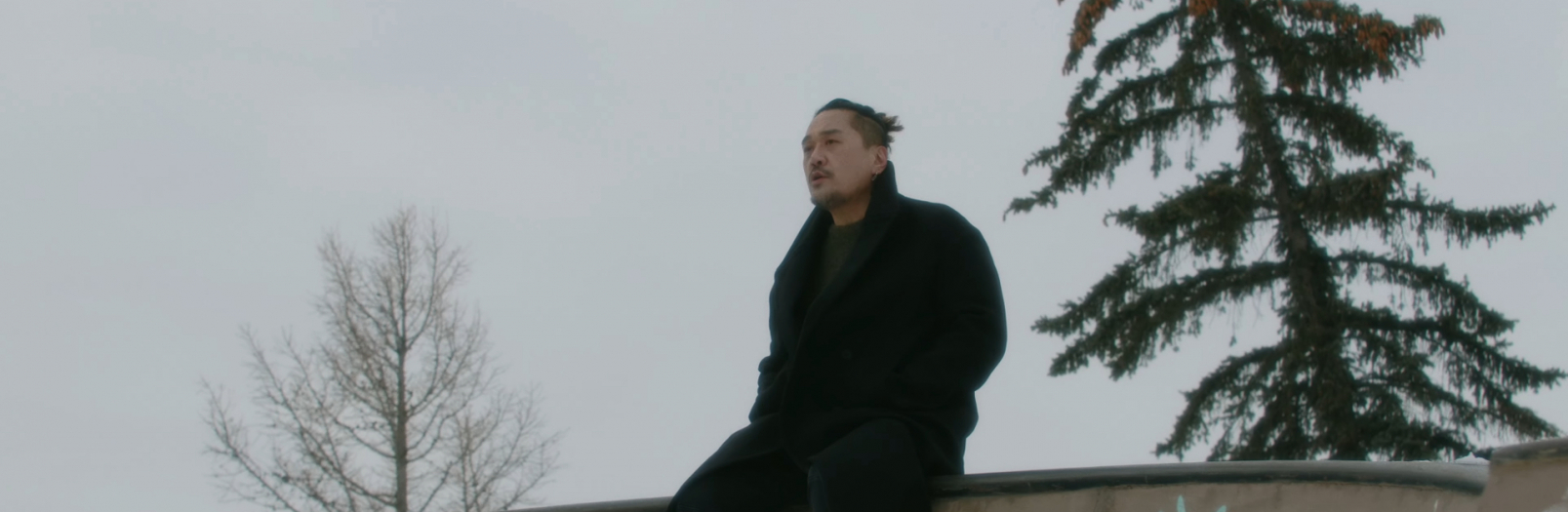 A Korean man sits on a wall wearing a winter coat.