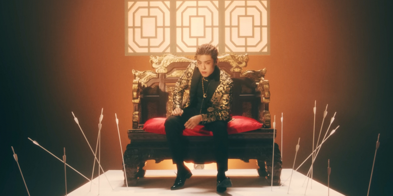 Image shows a Korean man sitting in a throne like love seat on a platform with arrows in the ground around him