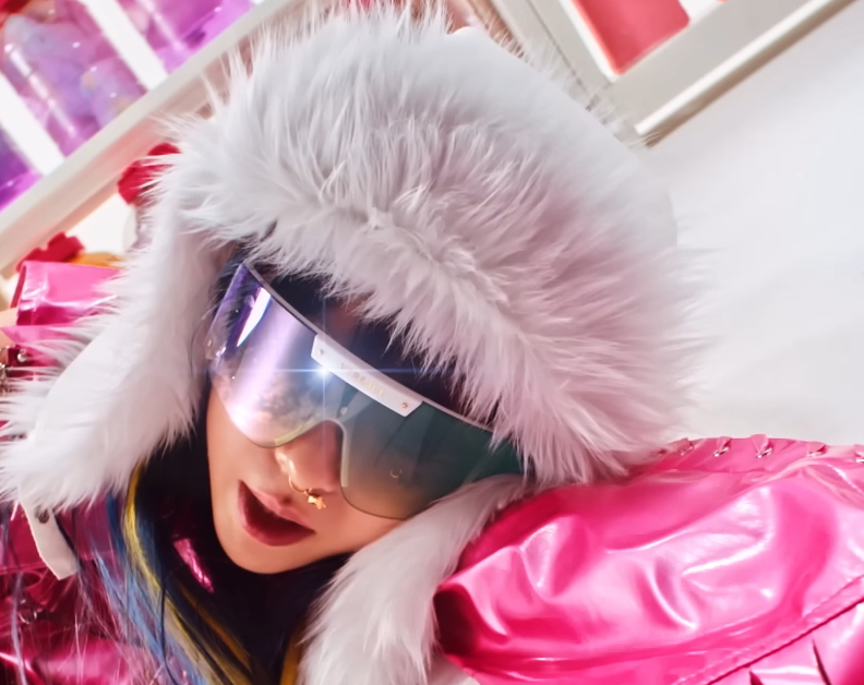 image shows a Korean women laying on a floor. She is wearing a fur hoodie, oversized sunglasses, and a pink vinyl coat