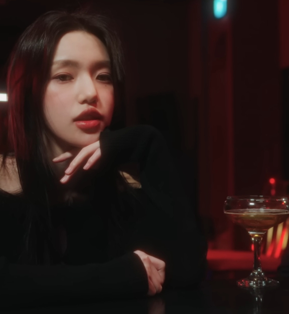 Image shows K-Pop singer iiso sitting at a bar with a man sitting next to her. 2 drinks are on the bar