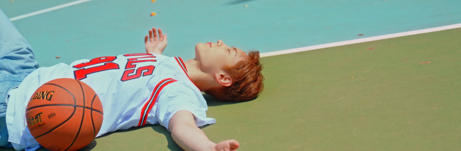 Yeong Seobin is laying down flat on his back on a basketball court. He is wearing a Chicago Bulls Jersey, and a basketball is laying next to him