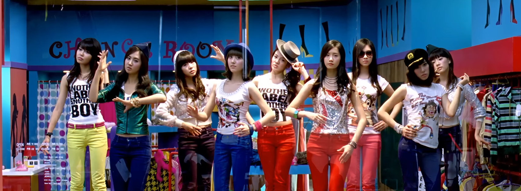 9 members of Girls' Generation are standing on pedestals in a storefront display window posing like mannequins.