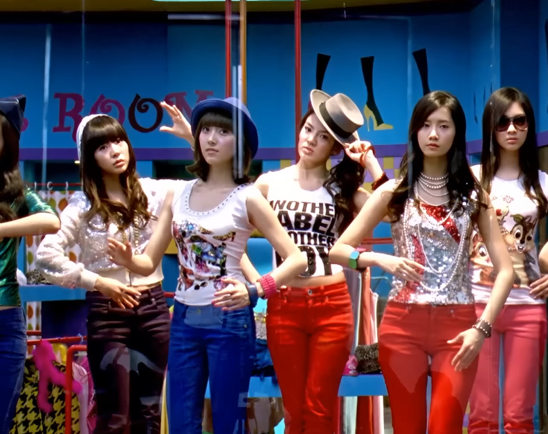 9 members of Girls' Generation are standing on pedestals in a storefront display window posing like mannequins.