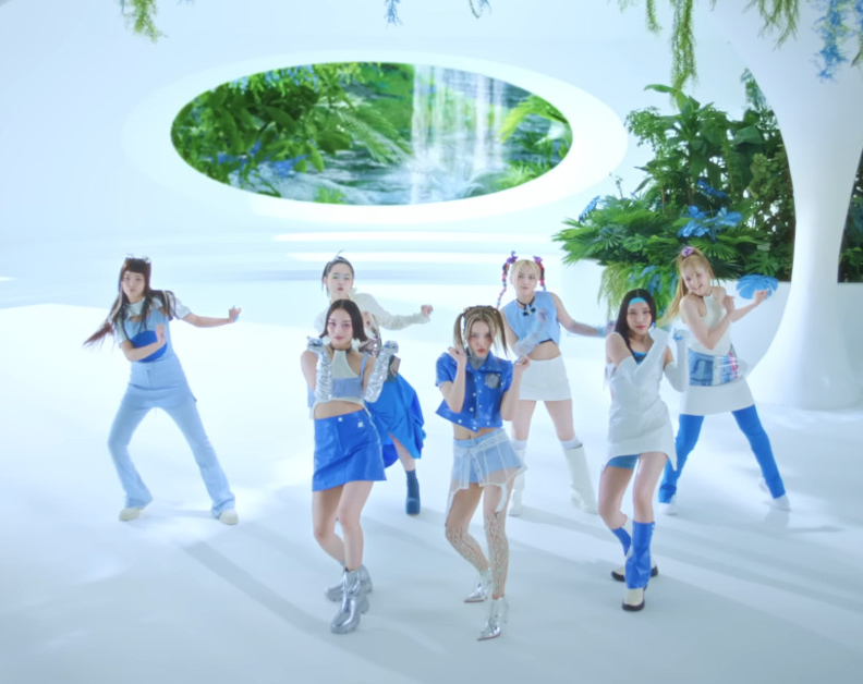 7 members of girl group, XG, are dancing in an all white building. You can see through open spaces fauna and water in the background.