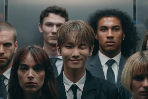 Singer KEY is standing in a crowded elevator winking at the camera