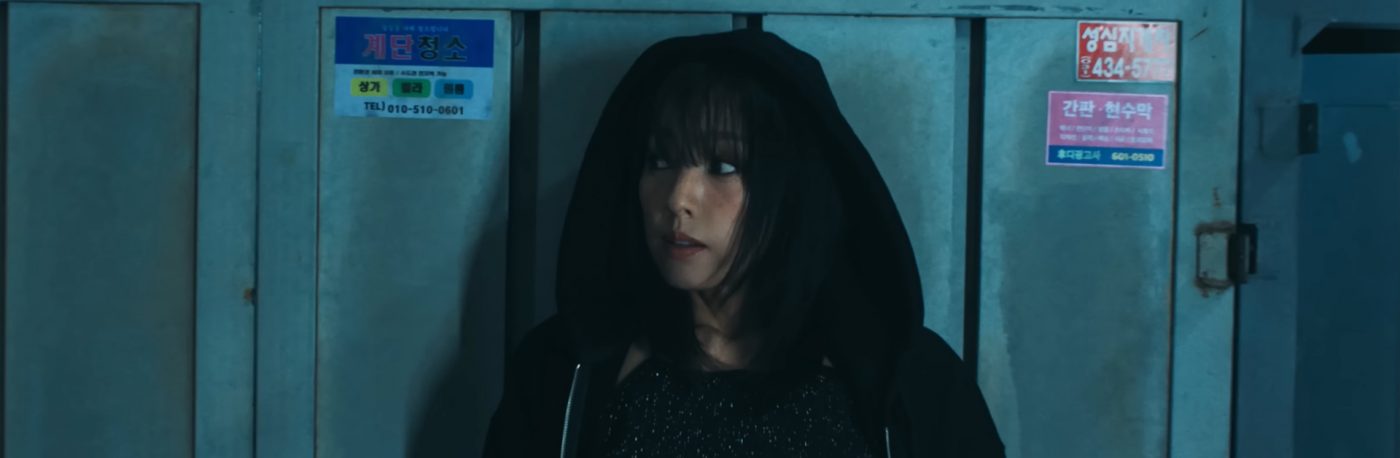 Lee Hyori is wearing a hoodie with the hood over her head, and is leaning against a wall