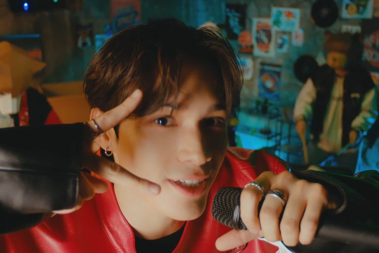 Singer Jay Chang is close to the camera holding a microphone and throwing up a peace sign. Behind him are band members wearing animal masks