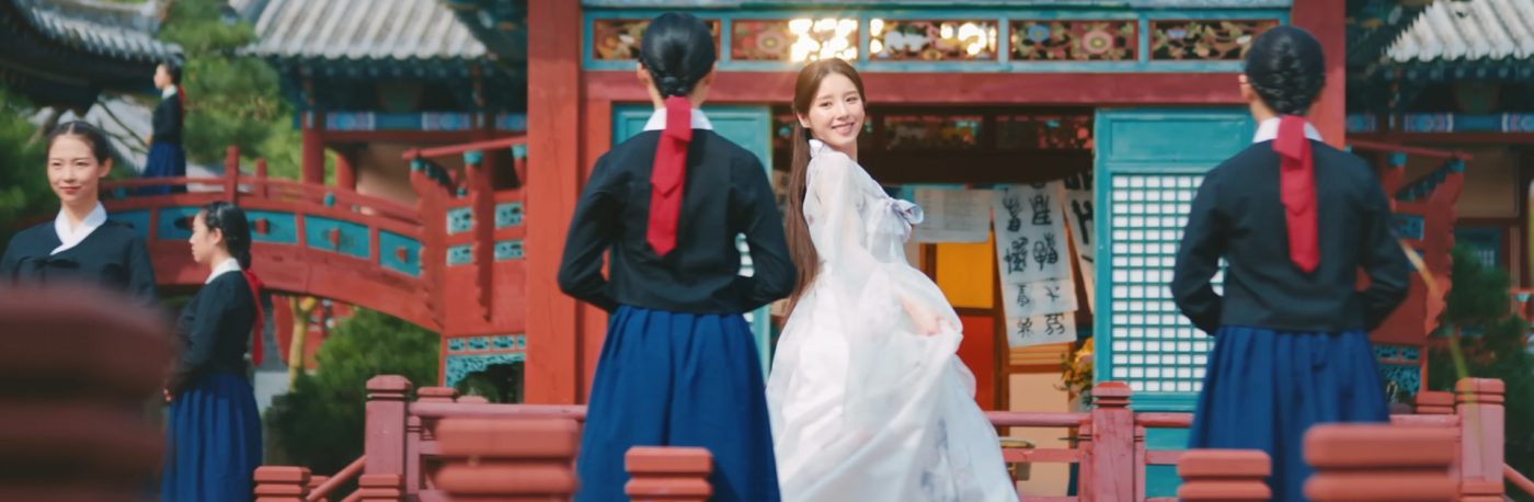 HeeJin is wearing a white hanbok in a Korean Temple. There are other women wearing hanbok around her