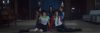 5 members of Red Velvet are sitting and kneeling together in a dimly lit room