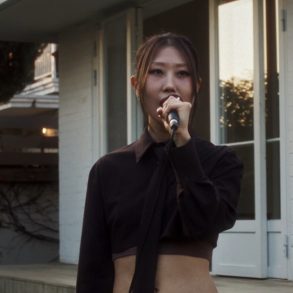 Singer g0nny is standing in the backyard of a home and singing in to a microphone