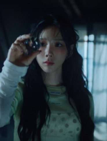 Singer Taeyeon is standing in a dark room room looking at a sphere in her hand