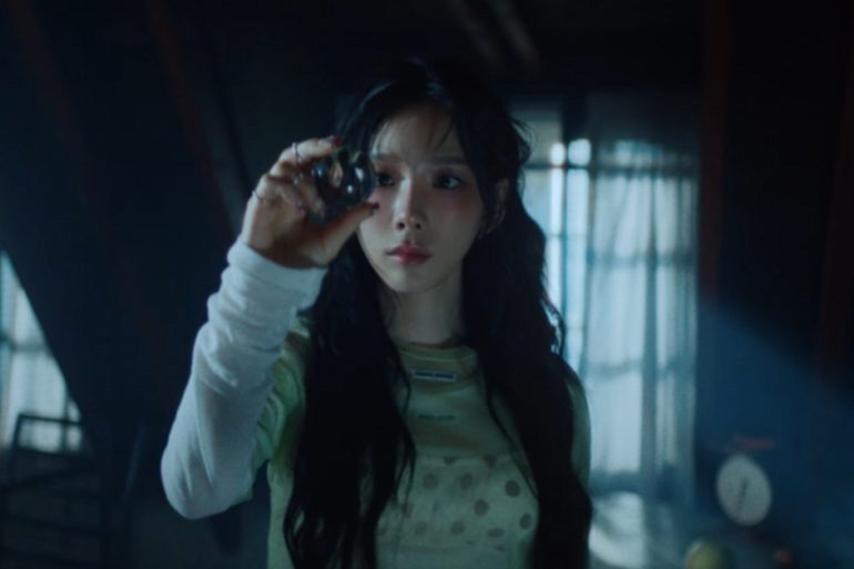 Singer Taeyeon is standing in a dark room room looking at a sphere in her hand