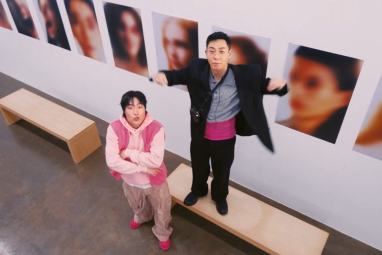 Jambino and Loco are in an art gallery. Jambino is standing with arms crossed, while Loco is standing on a bench