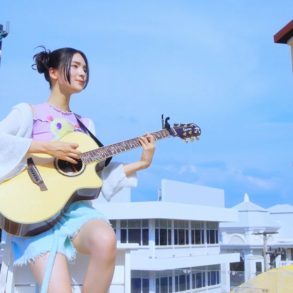 Gyubin is sitting on a small bench on a rooftop playing her guitar