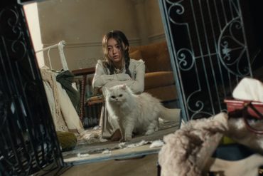 A reflection in the mirror shows YooA sitting on the floor of a messy room with a white cat