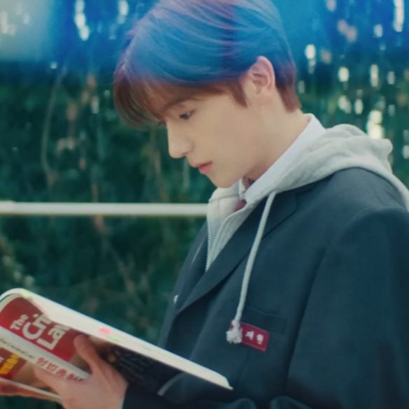 One of the members of THE BOYZ is standing outside in front of some pull up bars reading a book