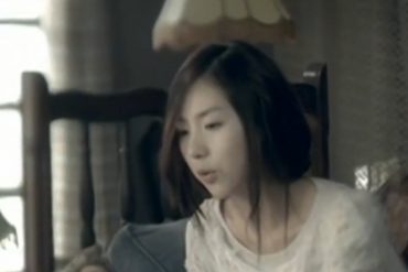 Kan MiYoun is singing while sitting on a bed