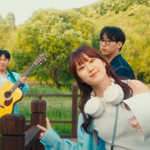 Woo Yerin is giving peace signs while standing on a wooden walkway. Behind her are 3 male band members