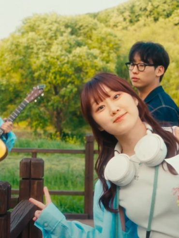 Woo Yerin is giving peace signs while standing on a wooden walkway. Behind her are 3 male band members