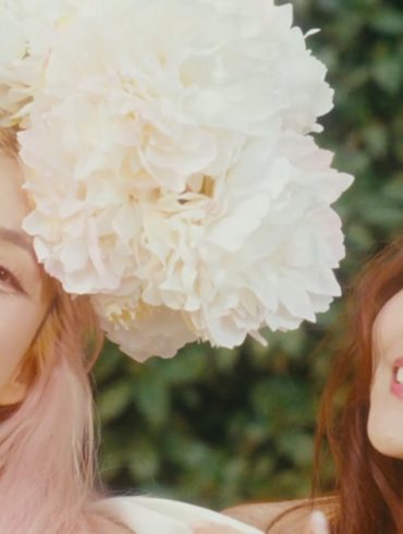 Bada and Eugene are smiling and looking at the camera. Both are wearing large flowers on their head
