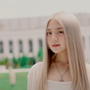 BORA B is standing in front of a wide building looking at the camera with a slight smile forming