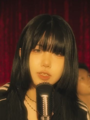 Korea music artist 200 is standing in front of a microphone performing while 2 guys are dancing behind her