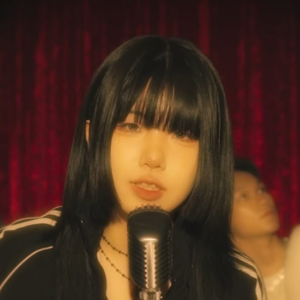 Korea music artist 200 is standing in front of a microphone performing while 2 guys are dancing behind her